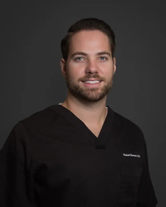 Man in black medical scrubs, smiling.